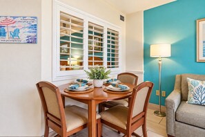 A dining area with a round table, four chairs, and a window with blinds. - Beach Cove Resort 308 (North Myrtle Beach)