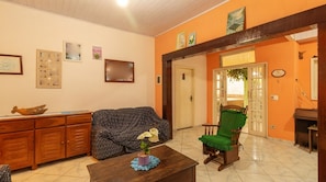 A living room with a sofa, a wooden cabinet, a green chair, and a small table with a plant. - House with Pool and BBQ in Rio Escuro (Ubatuba)