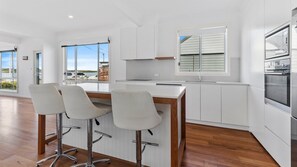A modern kitchen with white cabinetry, a wooden countertop, and a built-in oven. There are three bar stools with metal legs. - Channel View by HolidayCo. (SWANSEA)