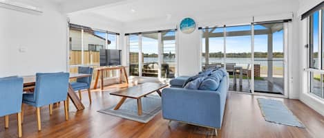 A spacious living area with a sofa, chairs, a coffee table, and a TV. Large windows offer a view of a body of water.