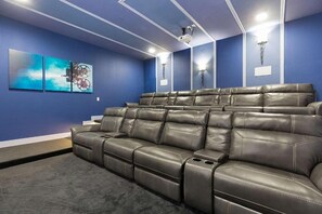 Ein Heimkinozimmer mit einer großen, hochverstellbaren Ledersofa, blauen Wänden und einem an der Decke befestigten Projektor.