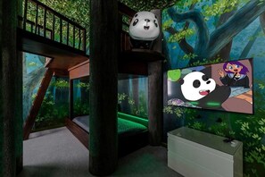 Une chambre avec un lit superposé, un écran de télévision diffusant des dessins animés et une fresque murale sur le thème de la forêt.
