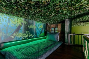 Ein Zimmer mit einem Bett, einem Fenster und einer Wand mit einer deckenhohen, von Blättern bedeckten Wandgestaltung.