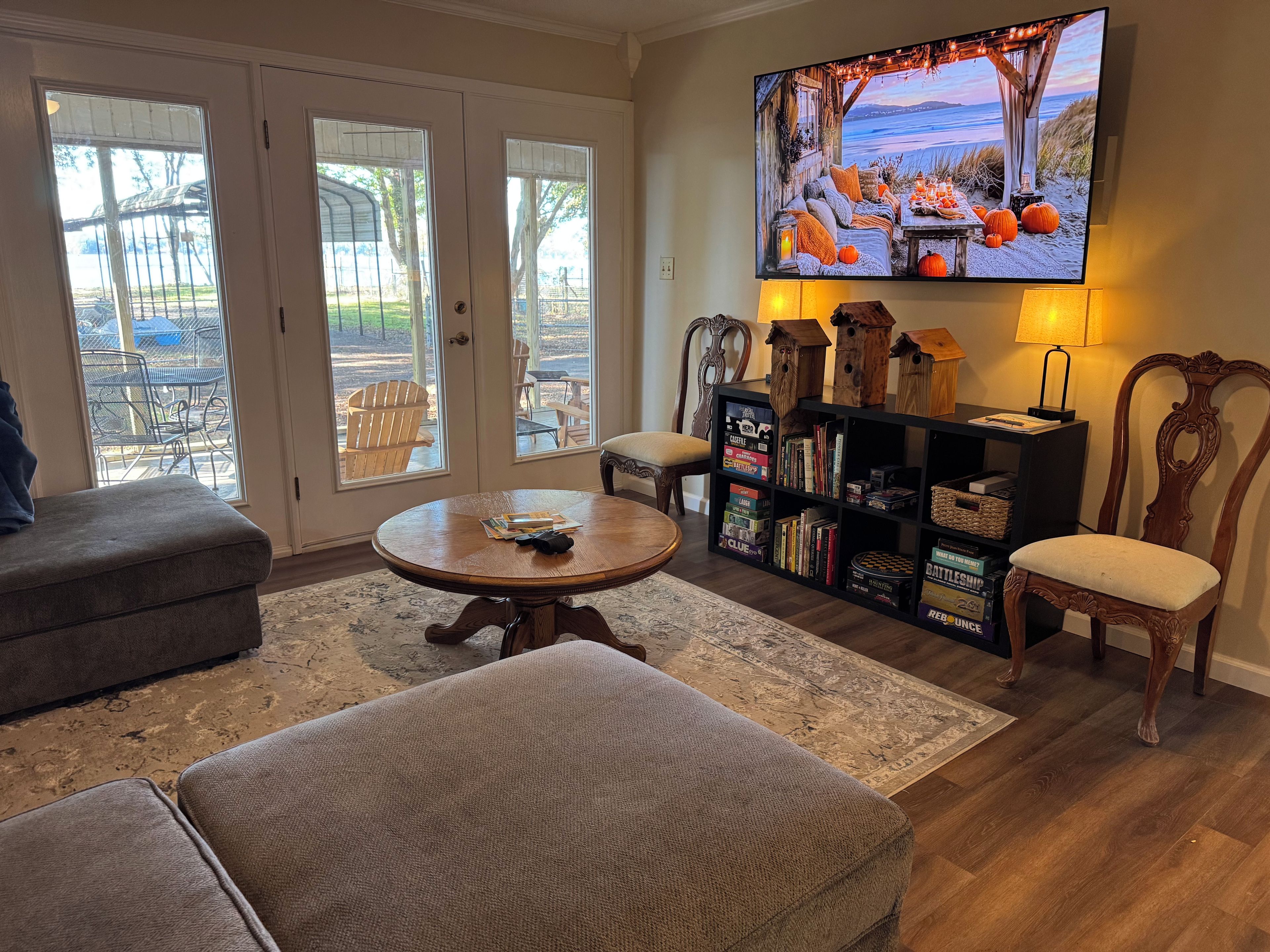 A living room with a television, ottomans, a bookshelf, and a view through the glass doors.