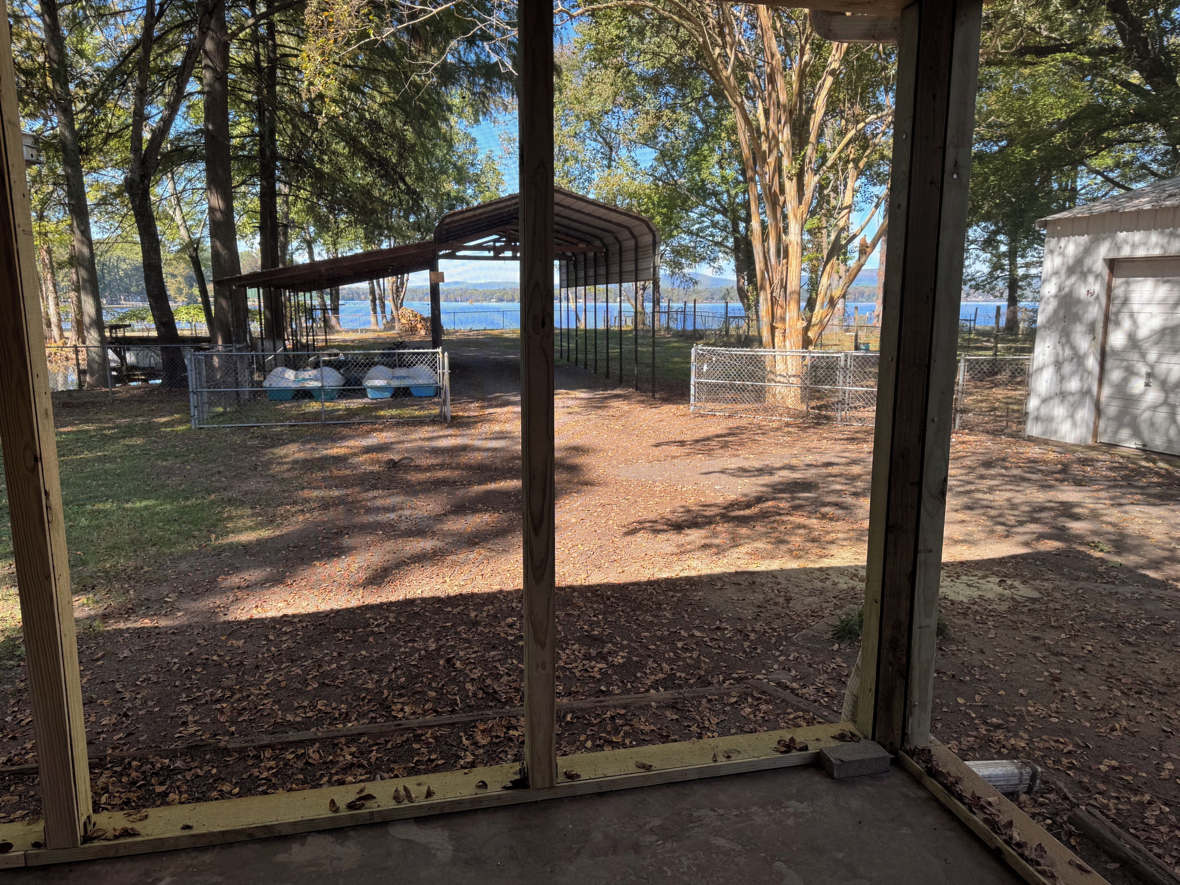 A fenced outdoor area with a covered seating area, a small shed, and a view of a body of water.