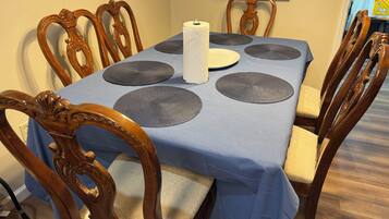 A dining table with a blue tablecloth, six matching placemats, a white paper towel dispenser, and wooden chairs with intricate carvings.