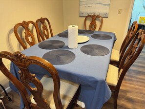 Una mesa de comedor con mantel azul, seis individuales a juego, un dispensador de servilletas de papel blanco y sillas de madera con intrincados relieves.