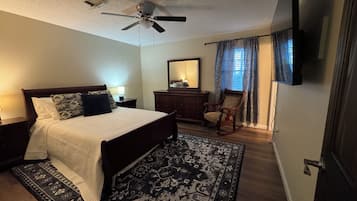 A bedroom with a bed, a dresser, a chair, a ceiling fan, and a television.