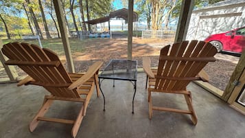 Two wooden Adirondack chairs facing a metal table and a view of a park with a covered area and a red car parked outside.
