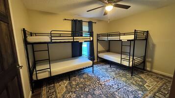 A room with bunk beds, a ceiling fan, and a patterned rug.