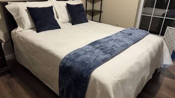 A bed with a white quilt and a dark blue throw blanket.
