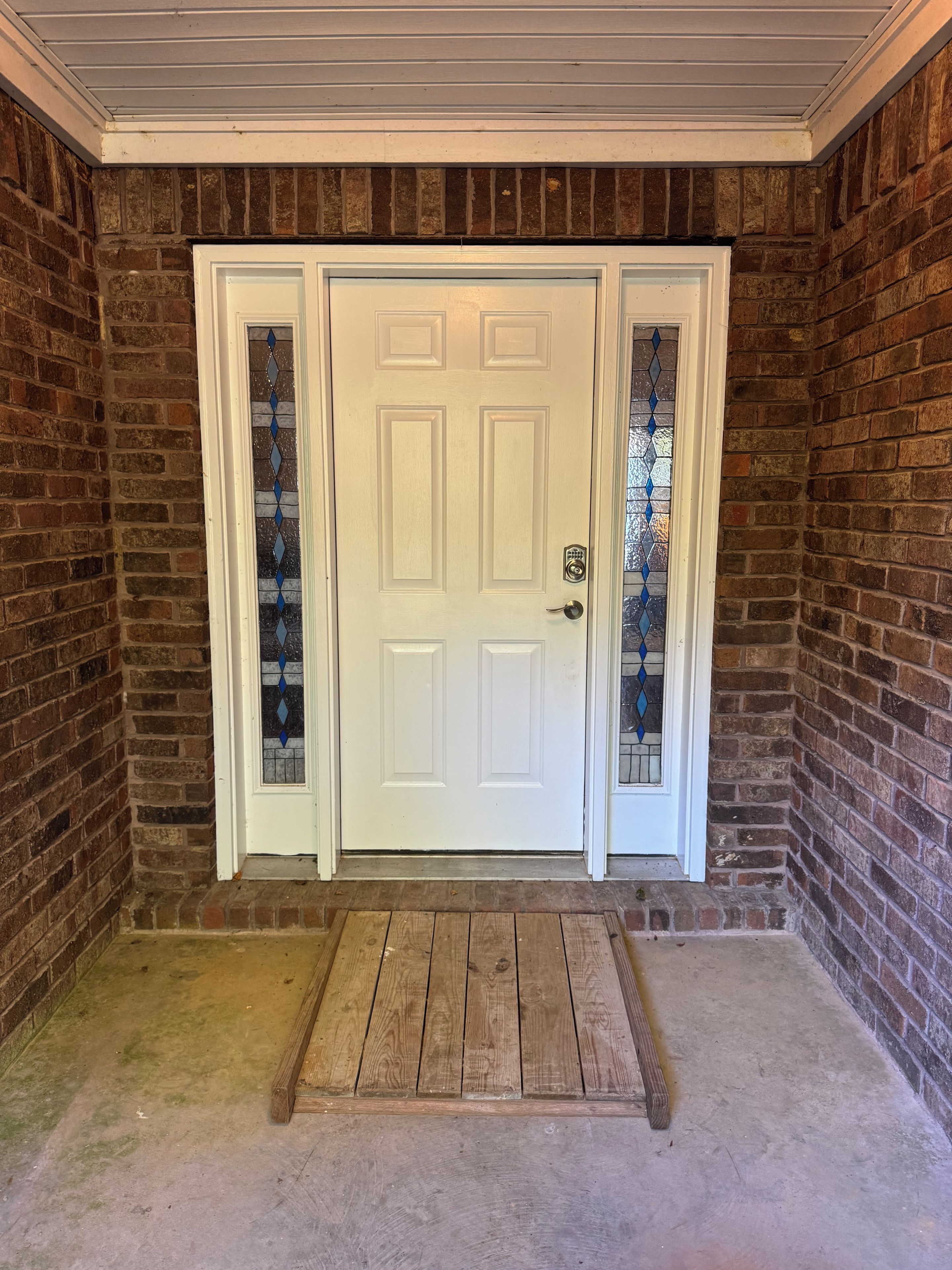 A white door with a glass panel, set in a brick wall with a wooden floor and a concrete floor.