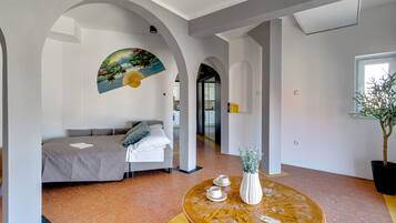 Una habitación moderna con una cama, una mesa redonda de madera con tazas y un florero, y un cuadro en la pared.