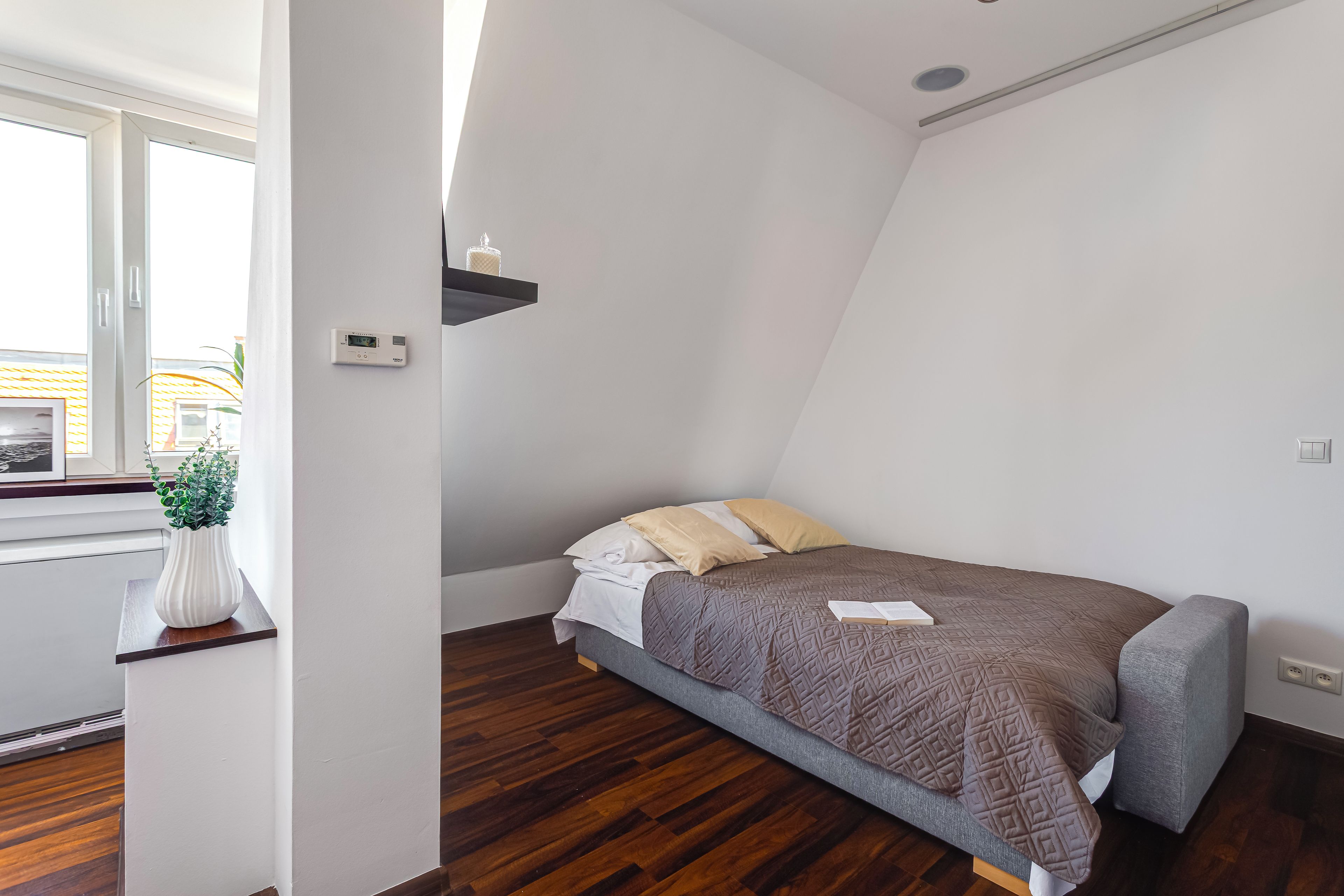 Un dormitorio con cama, mesita de noche, planta en maceta y ventana.