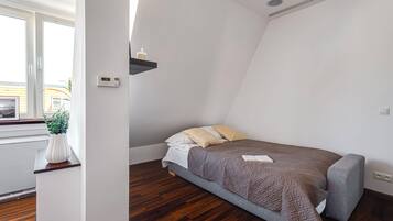 Un dormitorio con cama, mesita de noche, planta en maceta y ventana.