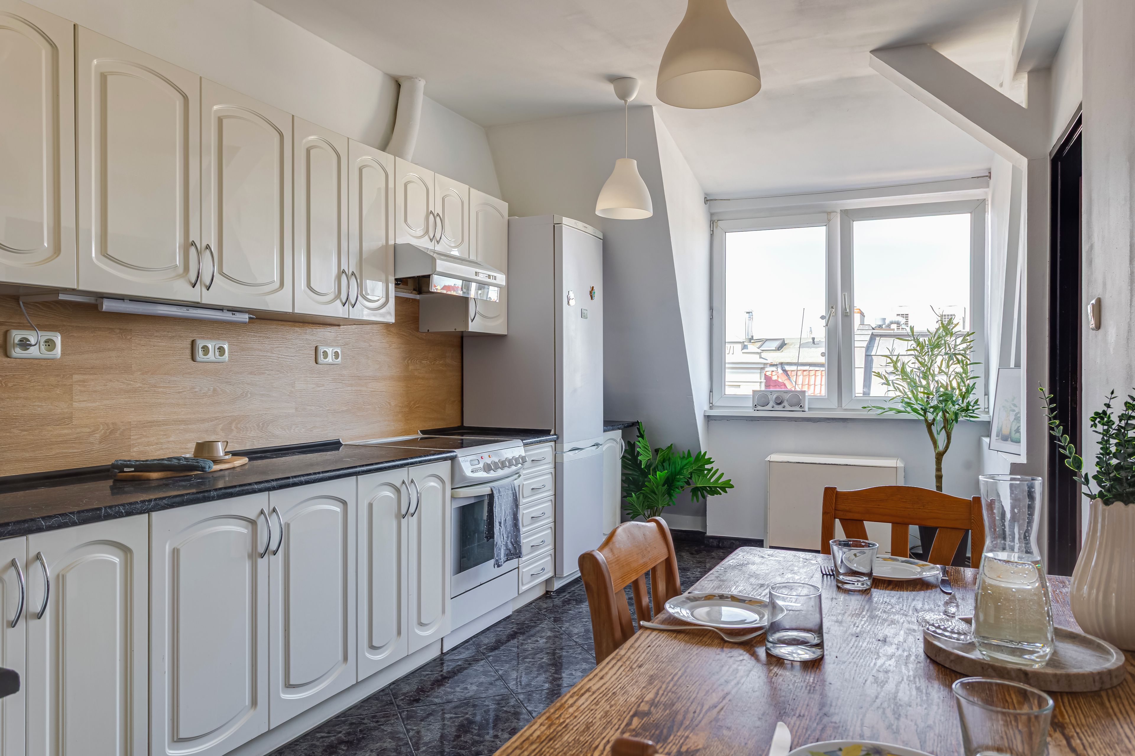 Una cocina moderna con armarios blancos, encimera negra y un comedor con mesa y sillas de madera.