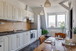 A modern kitchen with white cabinets, a black countertop, and a dining area with a wooden table and chairs. - Widok na Ratusz  3 min na Rynek (Poznań)