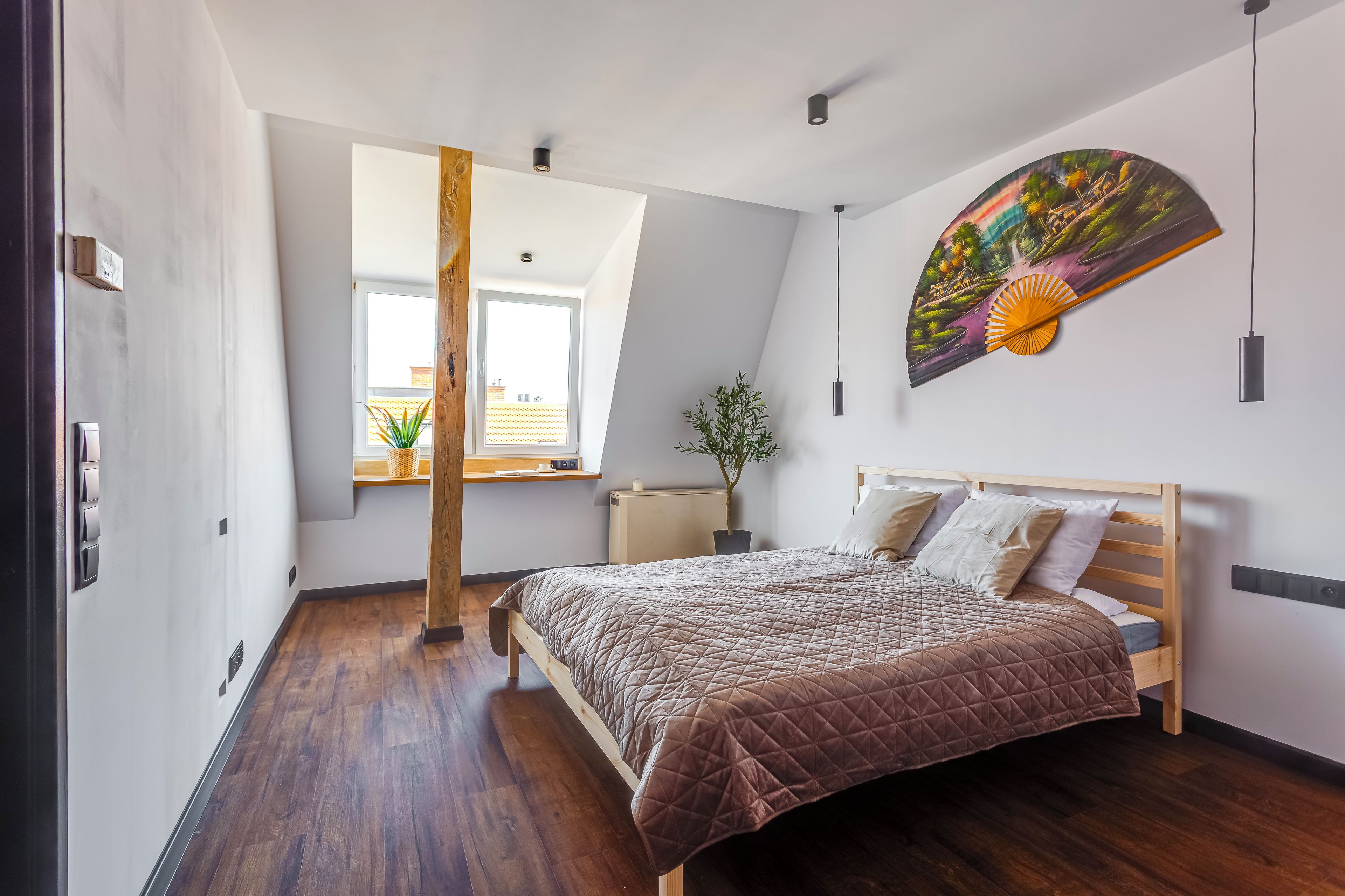 Un dormitorio con cama, ventana, radiador y un ventilador de pared.