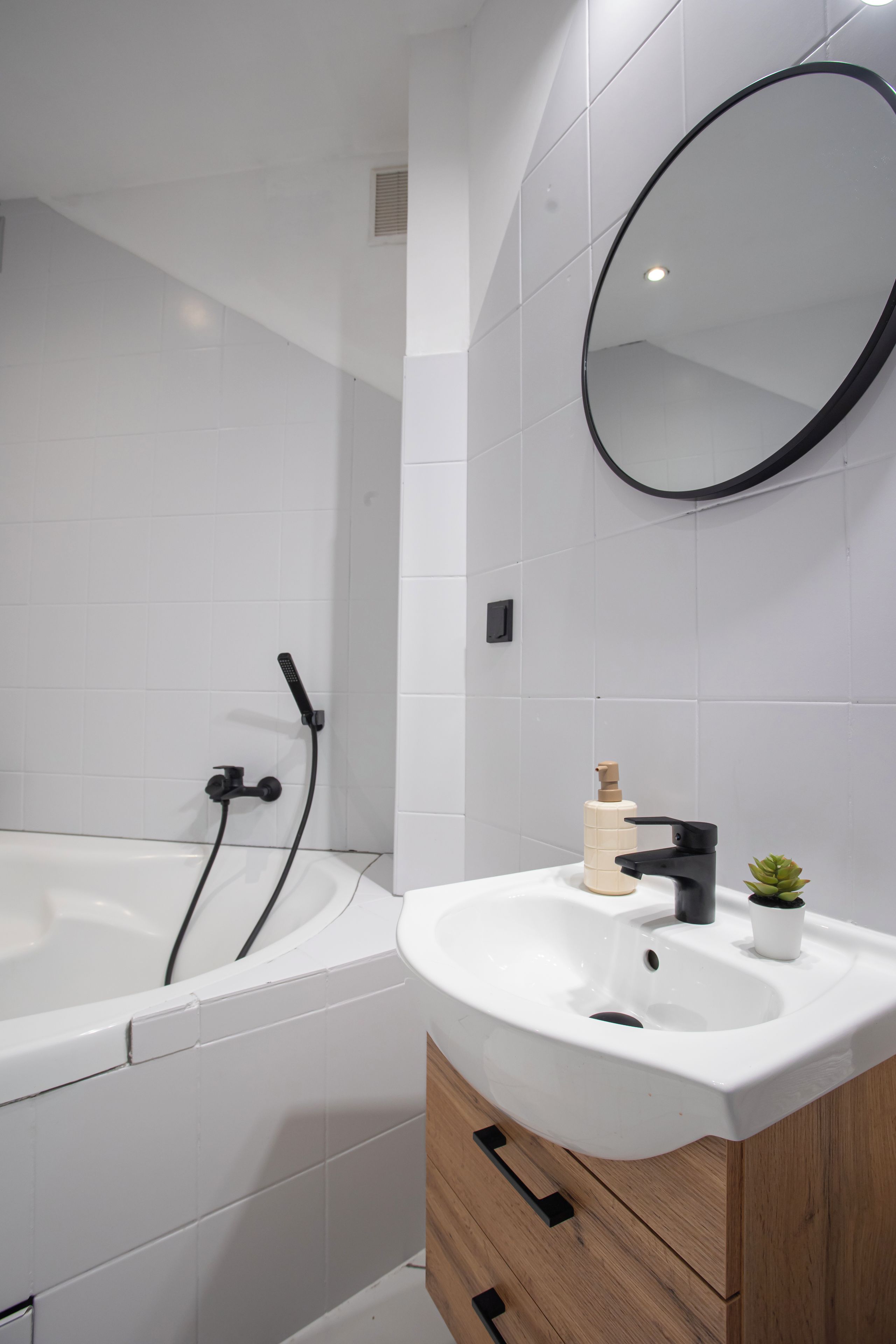 A modern bathroom with a white bathtub, a round mirror, and a wooden vanity with a sink.