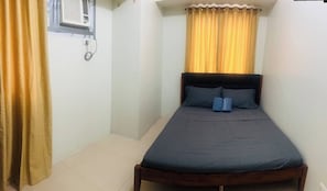 A small, single-bed room with a wooden headboard, a window with yellow curtains, and a wall-mounted air conditioning unit. - A Cozy 1BR 40sqm in Mandaluyong With City View (Mandaluyong)