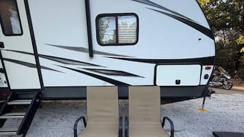 A recreational vehicle with a kitchen area, a table with chairs, and a gravel ground.