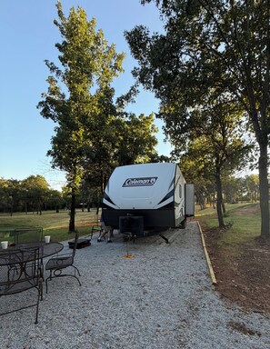 A Coleman RV parked on a gravel area with a metal table and chairs nearby.