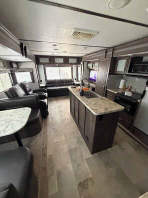 Un intérieur de camping-car compact comprenant un coin cuisine, un espace repas avec une table en marbre et un coin salon avec un canapé.
