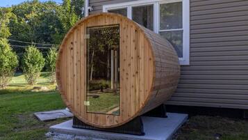Een houten sauna met een deur, op een betonnen fundering in de open lucht.