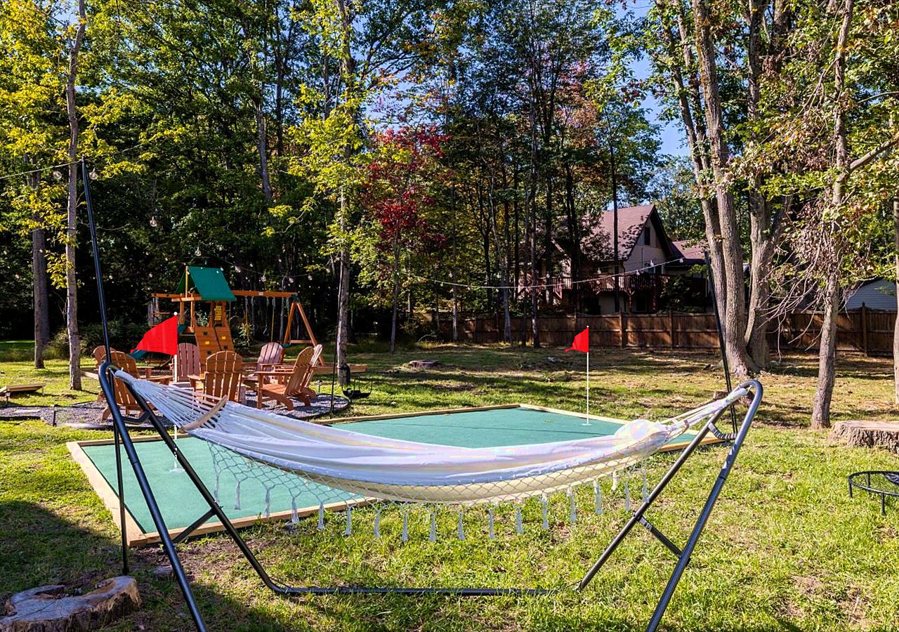 A hammock set up on a grassy lawn with a swing set and a wooden deck in the background.
