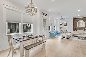 A spacious living room with a dining area, a chandelier, and a view of the outside. - Recovery Room (Santa Rosa Beach)