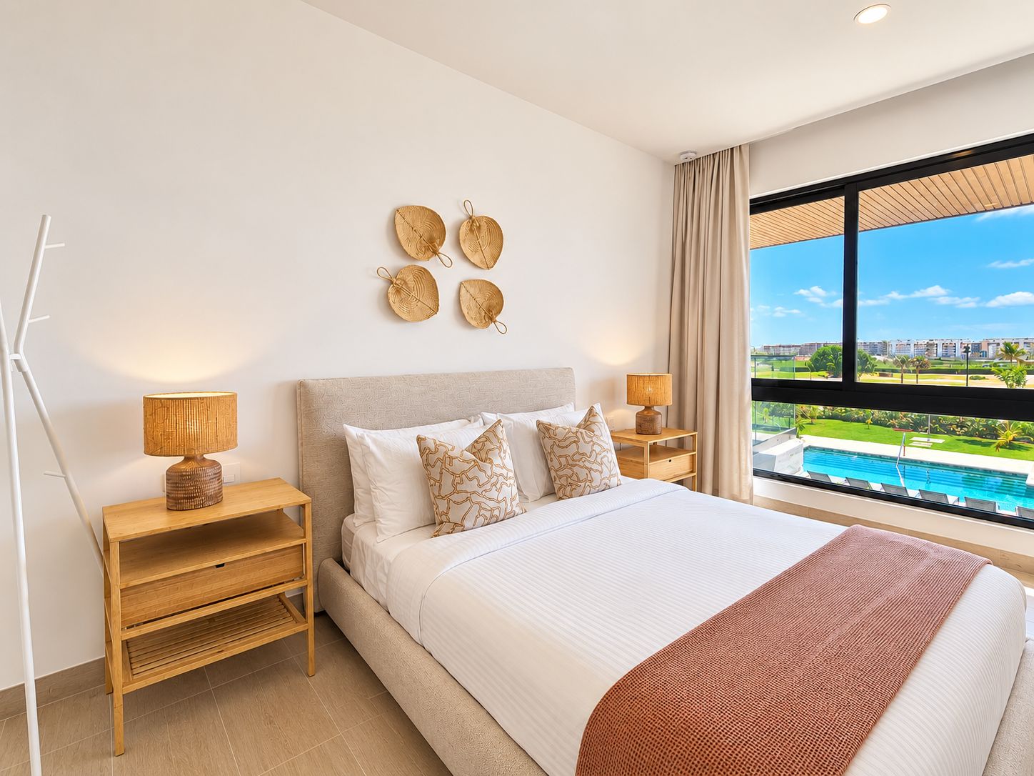 A hotel room with a large bed, two bedside tables, a view of a swimming pool, and a cityscape.