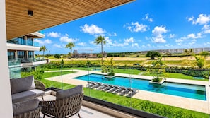 A balcony with a view of a swimming pool, lounge chairs, and a modern building.