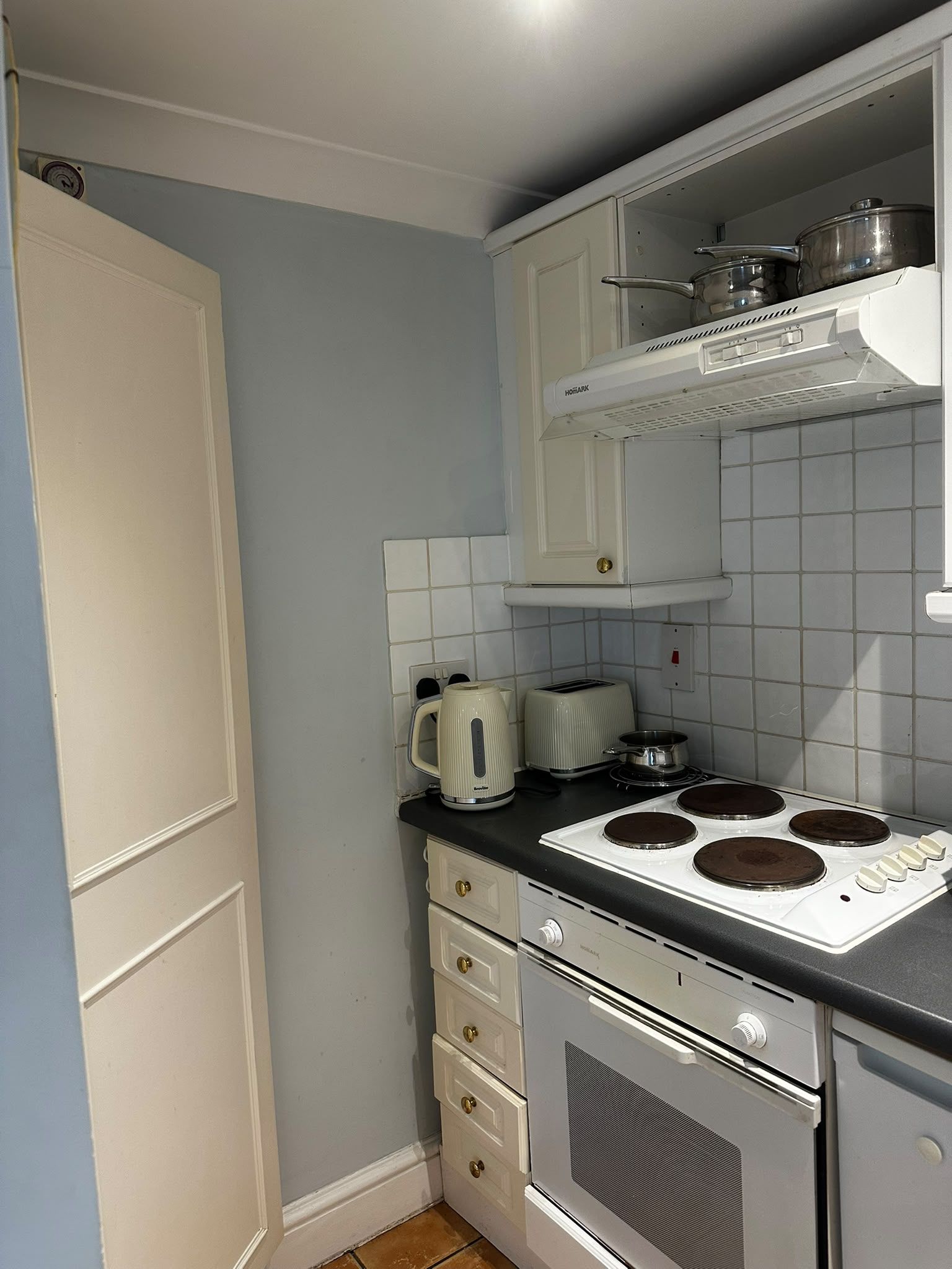 Ett kompakt kök med vita skåp, en spis, en vattenkokare och en brödrost.