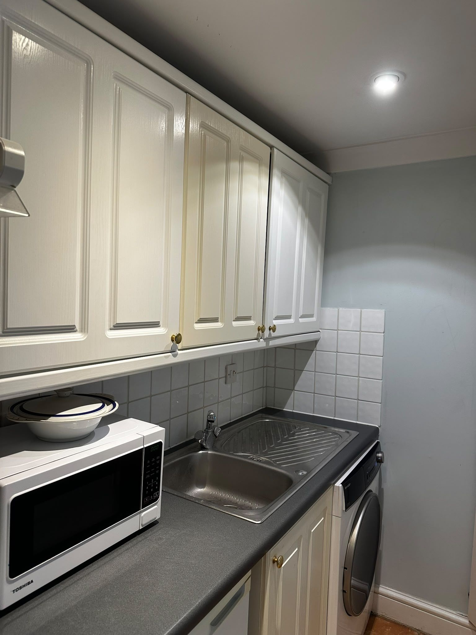 A kitchen with white cabinets, a microwave, a sink, and a washing machine.