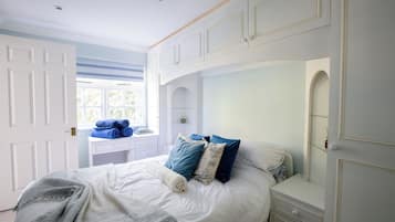 A bedroom with a bed, a bedside table, a mirror, and a window.