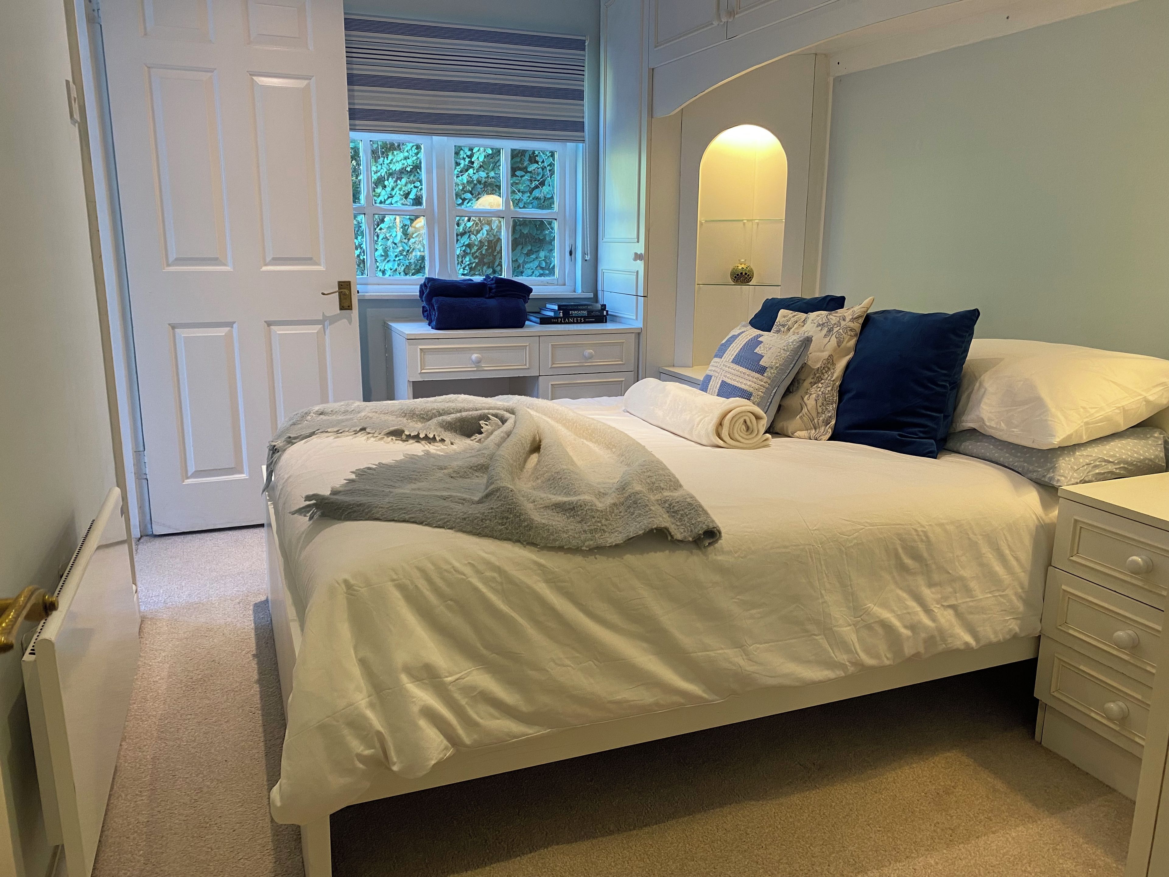 A bedroom with a bed, a bedside table, a window, and a door.