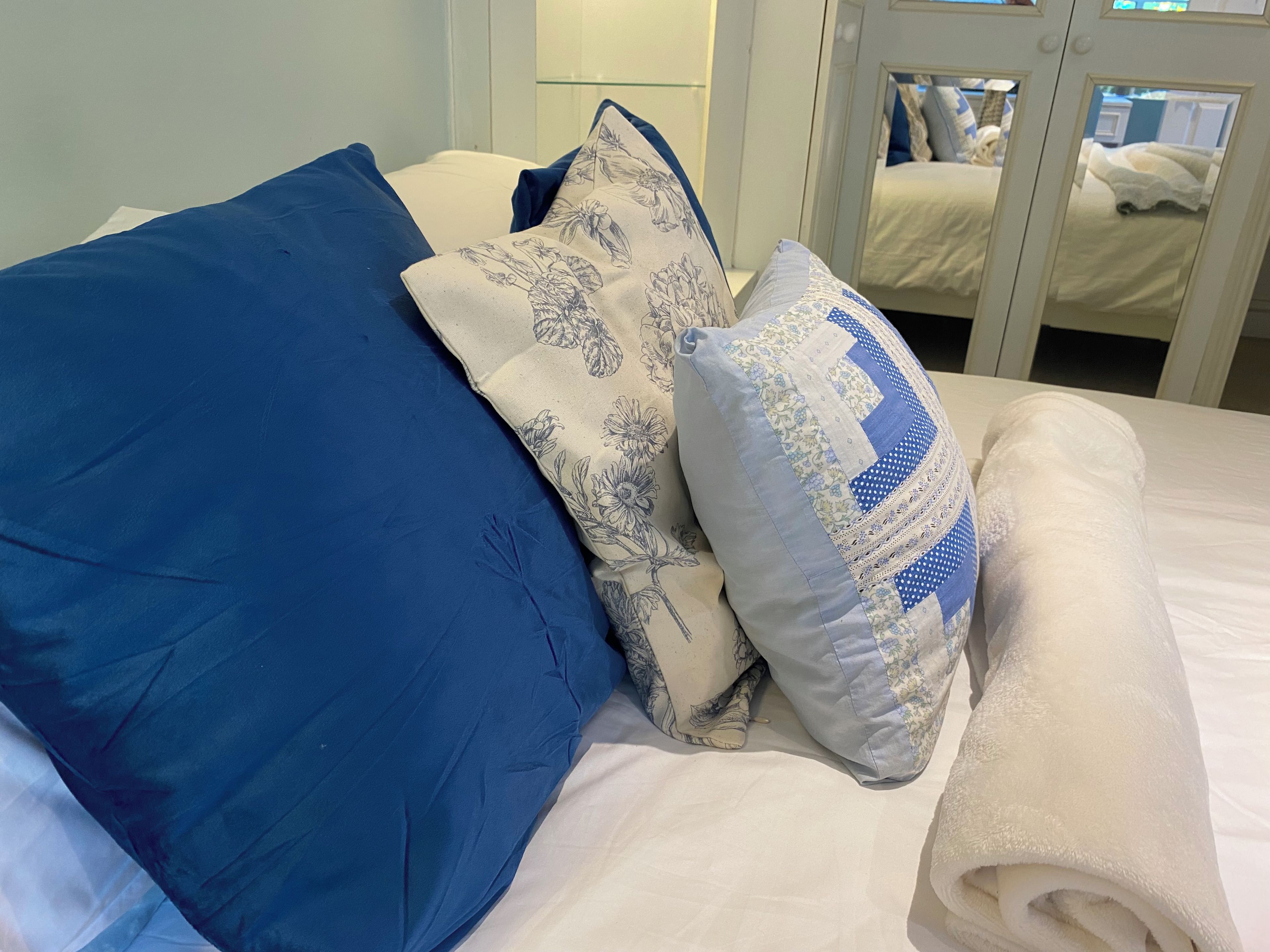 A bed with blue and white pillows, a white blanket, and a glass door leading to another room.