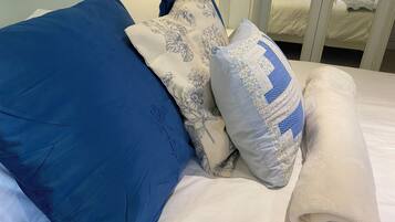 A bed with blue and white pillows, a white blanket, and a glass door leading to another room.