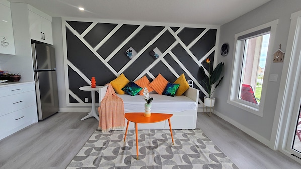 A modern kitchen with a built-in refrigerator, a dining area with a white sofa and orange accents, and a geometric-patterned rug. - Brand new 1200 sq ft spacious secondary suite, short drive from YYC airport. (Calgary)