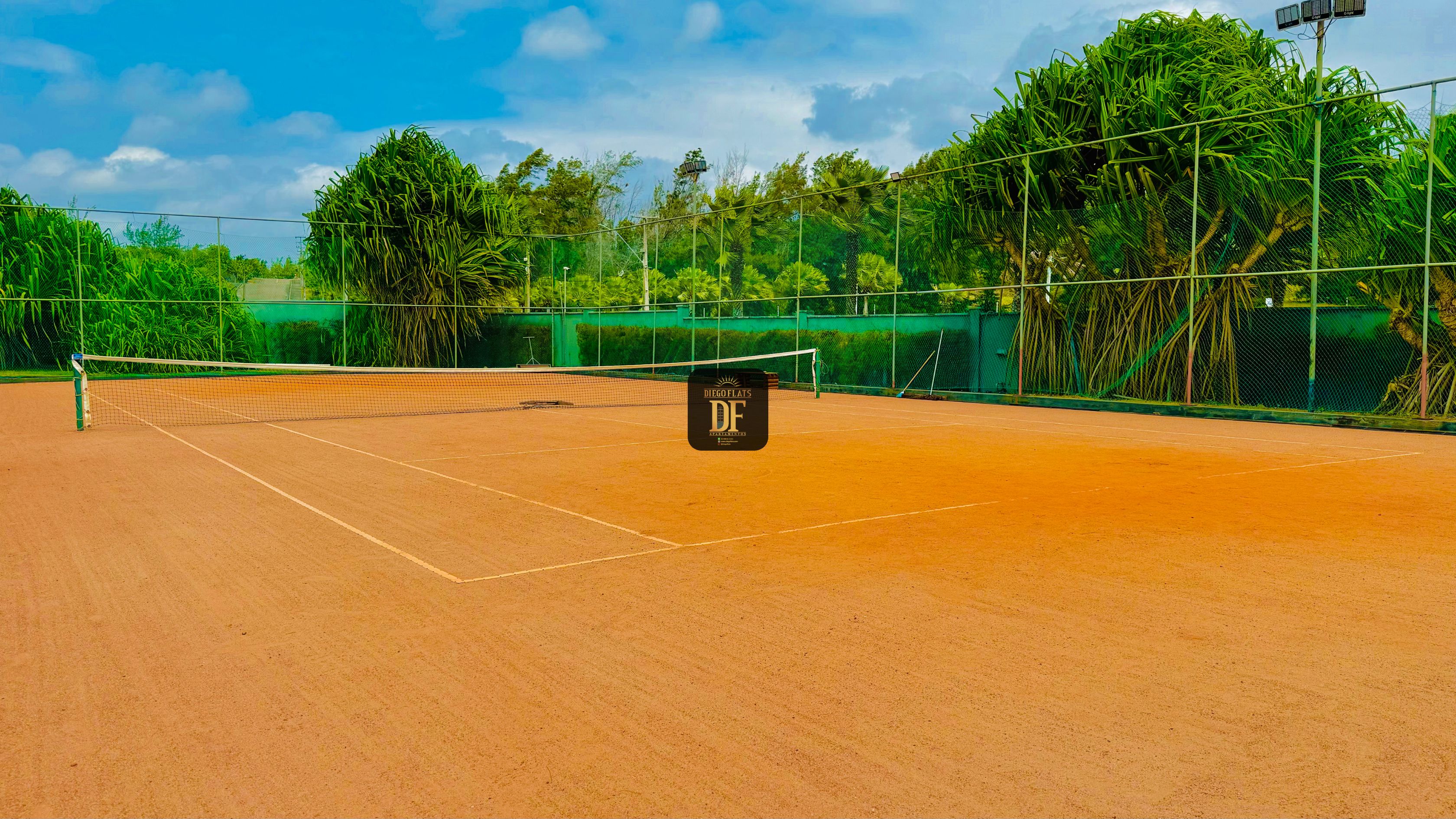 A tennis court with a net, surrounded by a fence and greenery.