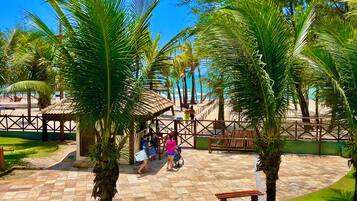 Un sendero pavimentado con palmeras, una zona de estar techada y una playa al fondo.