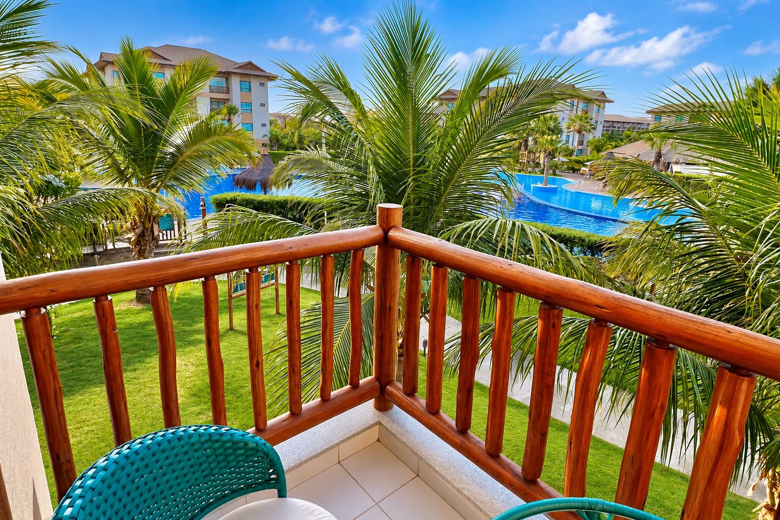 A balcony with a wooden railing, a green chair, and a view of a swimming pool and hotel buildings.
