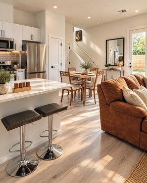 A modern kitchen with stainless steel appliances, a dining area with wooden chairs, and a brown leather sofa. - Austin Retreat - Game Room, Yard, Theatre, Garage (Austin)