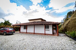 Una casa de dos pisos con techo de tejas, entrada de grava y un SUV rojo estacionado.