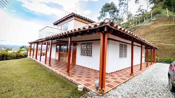 Una casa con un porche cubierto, un patio empedrado y vistas del paisaje circundante.
