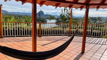 A hammock on a tiled patio with a view of a lake and mountains.