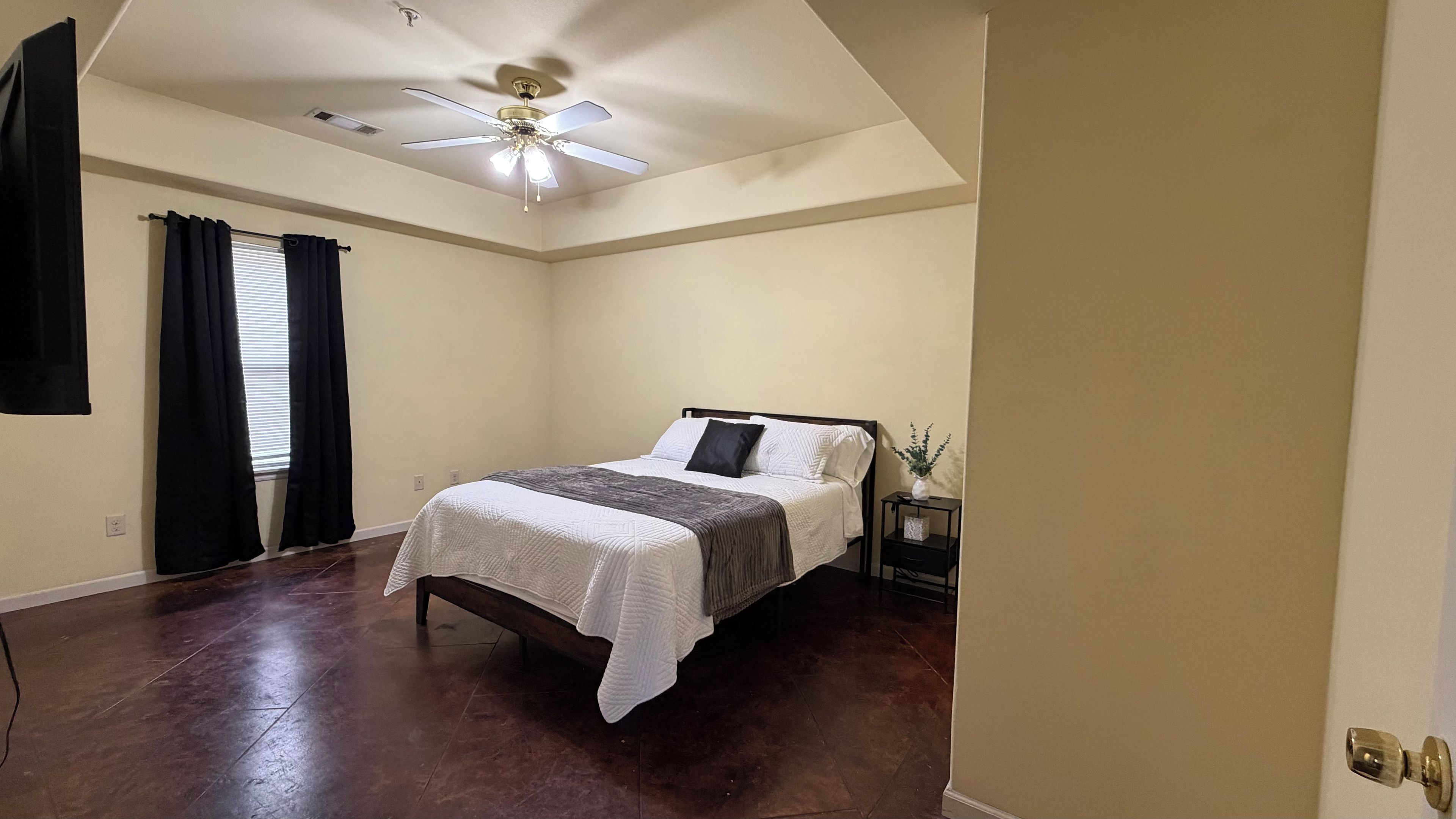 A bedroom with a bed, a nightstand, a ceiling fan, and a window with curtains.