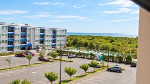 A multi-story hotel with a parking lot, a pool area with lounge chairs, and a view of the ocean. - ShoreLine | 2BR Coastal Condo + Pool (Brigantine)