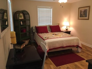 Un dormitorio con cama, mesita de noche, lámpara, estantería y ventana con persianas.