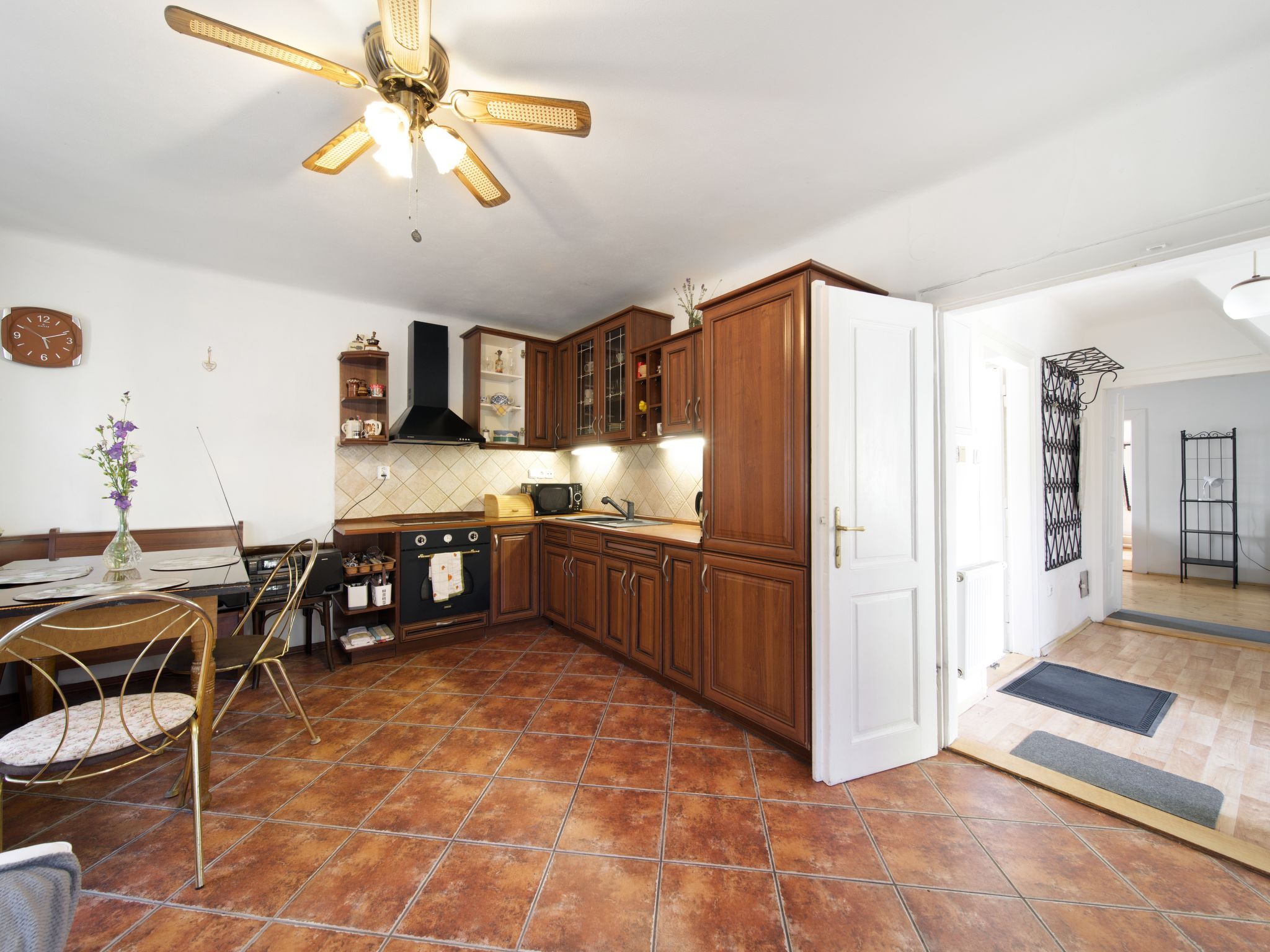 Une cuisine avec un sol carrelé, des meubles de rangement en bois, une cuisinière noire et un ventilateur de plafond.